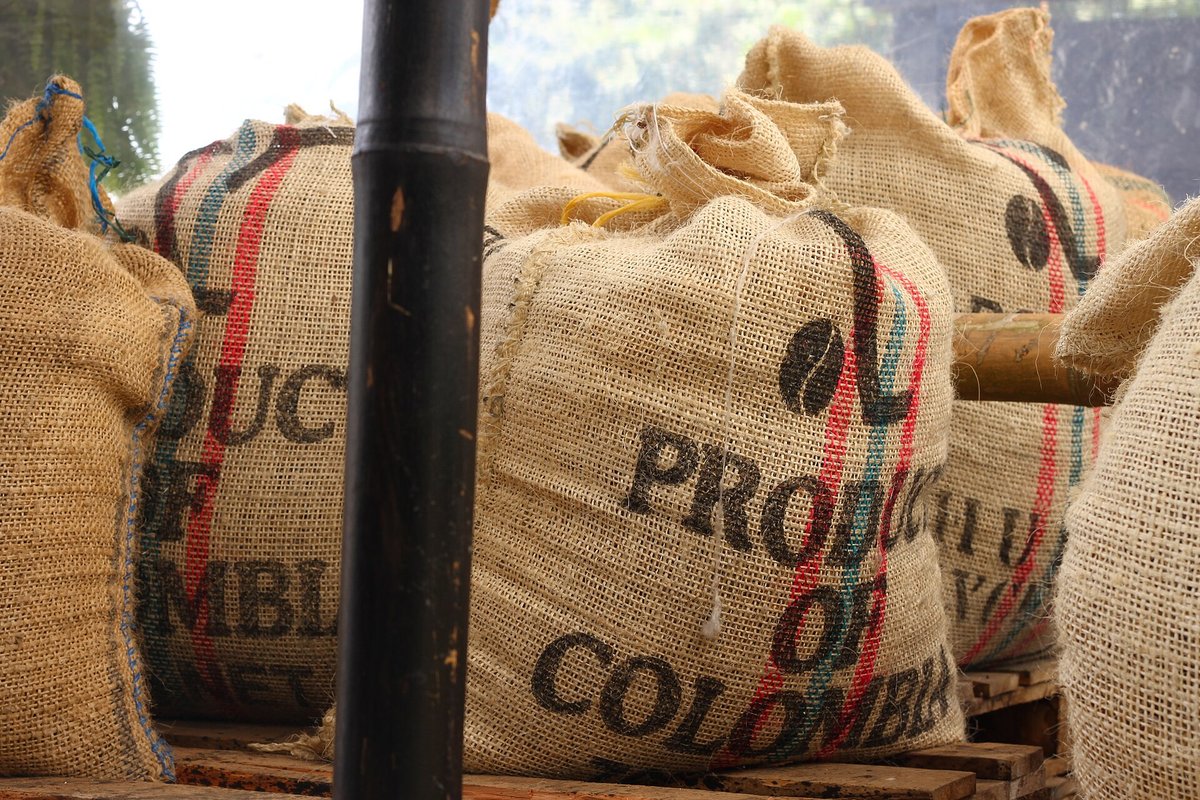 Jute sacks of green coffee stacked in a warehouse, printed in large letters PRODUCT OF COLOMBIA