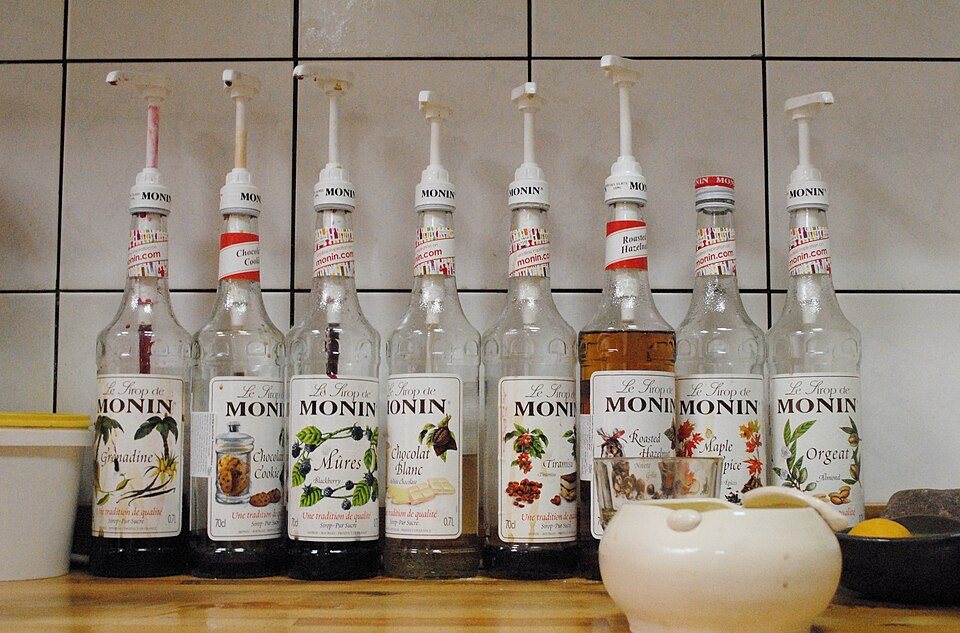 A row of flavored-syrup bottles fitted with pumps on a tiled café counter