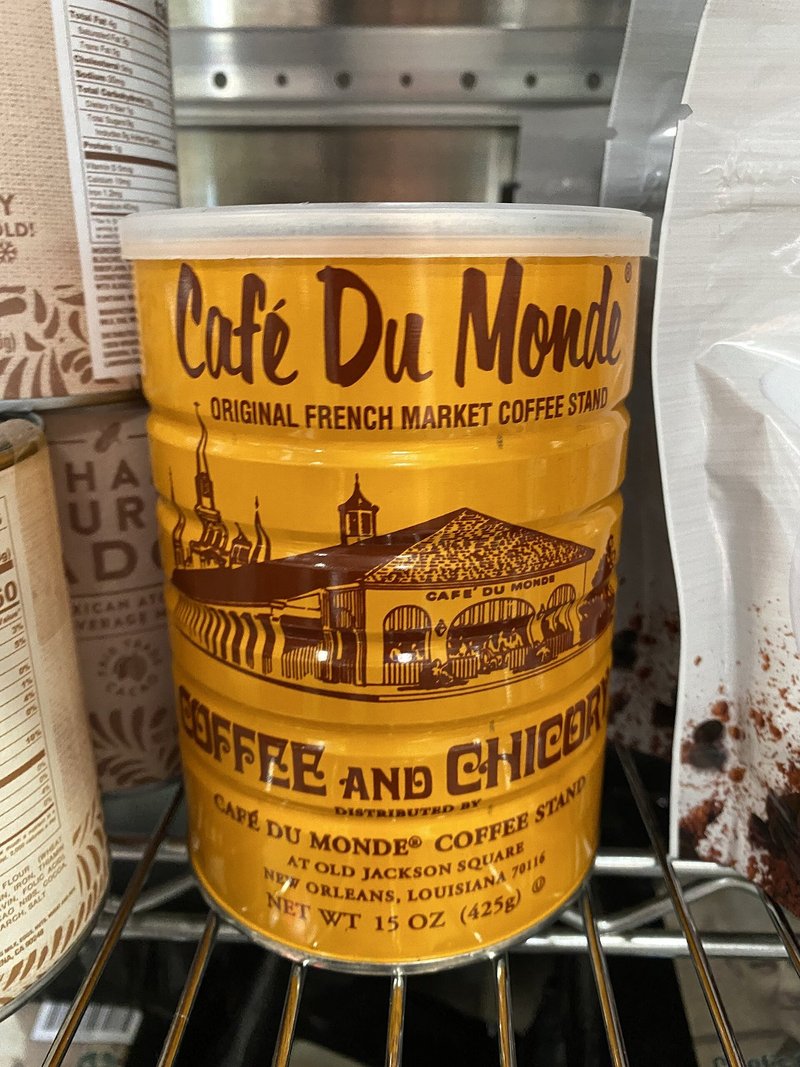 A tall yellow tin of Café du Monde coffee and chicory on a shop shelf, its label showing the French Market building
