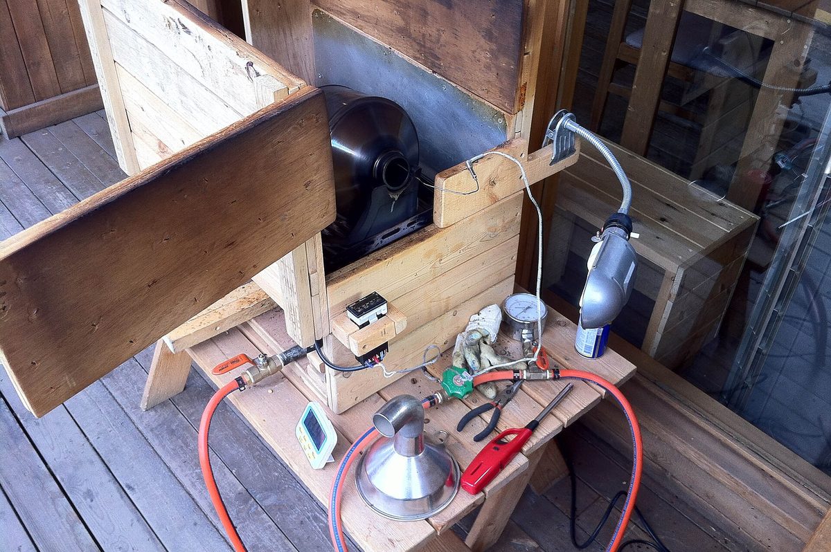 A stainless bowl of coffee beans mid-roast with a heat gun aimed down into it, chaff lifting off in the airflow