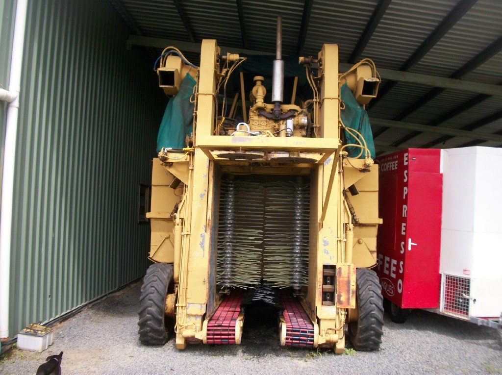 A large yellow mechanical coffee harvester parked in a shed
