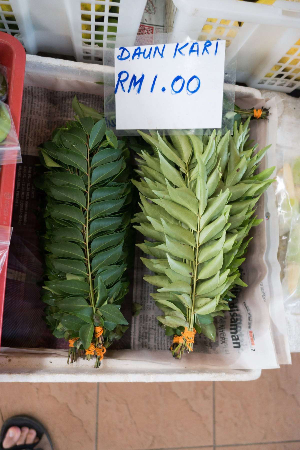 Bundles of fresh curry leaves for sale at a Malaysian market, labelled daun kari