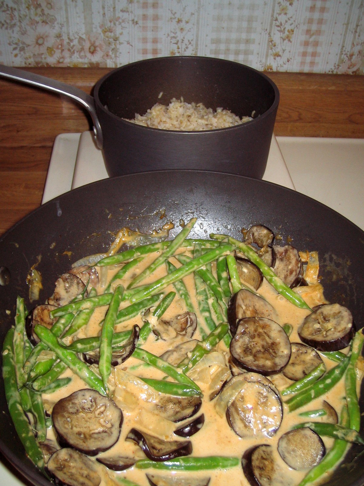 A red curry cooking in the wok with eggplant and long beans, the coconut milk gone pale orange from the paste