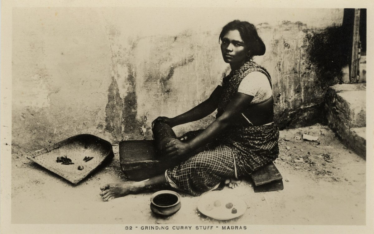 A historical photograph captioned "Grinding curry stuff, Madras" — a woman working spices on a flat stone slab with a stone roller