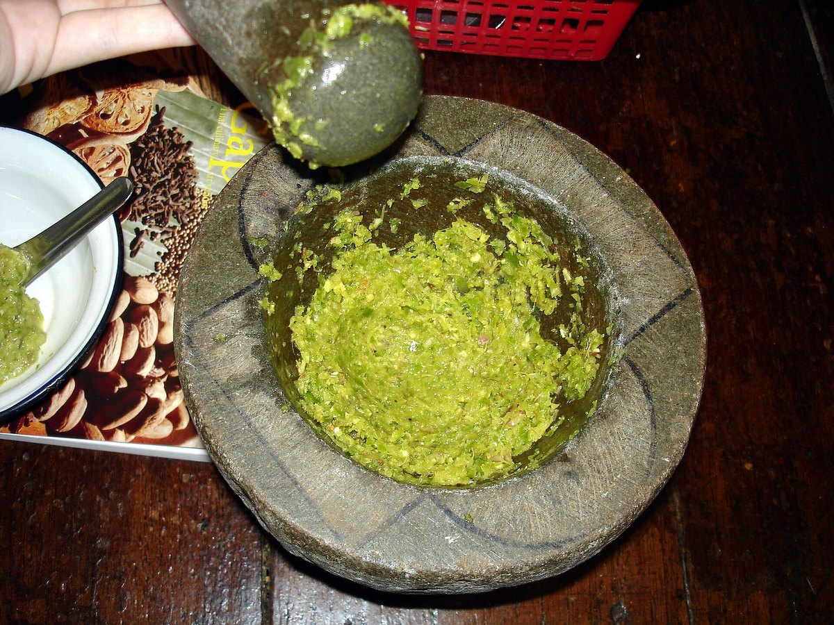 A granite mortar and pestle with a half-worked curry paste in it, aromatics still visible