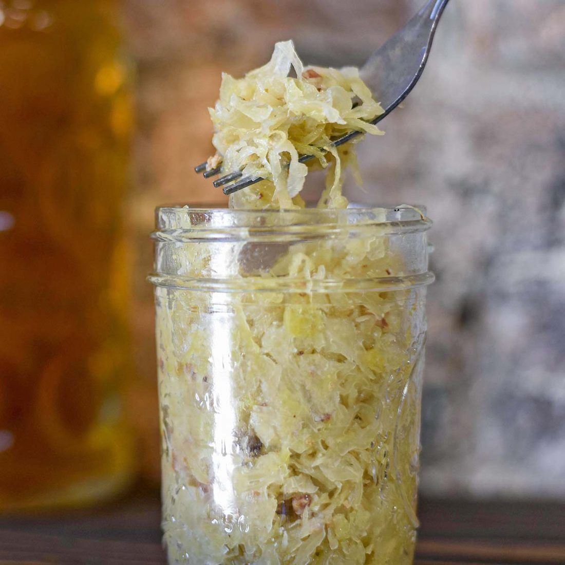 A forkful of sauerkraut lifted from a jar mid-ferment — cloudy brine, and the cabbage already going pale and translucent