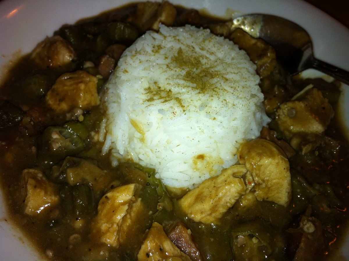 A dark gumbo with a mound of rice in the middle of it