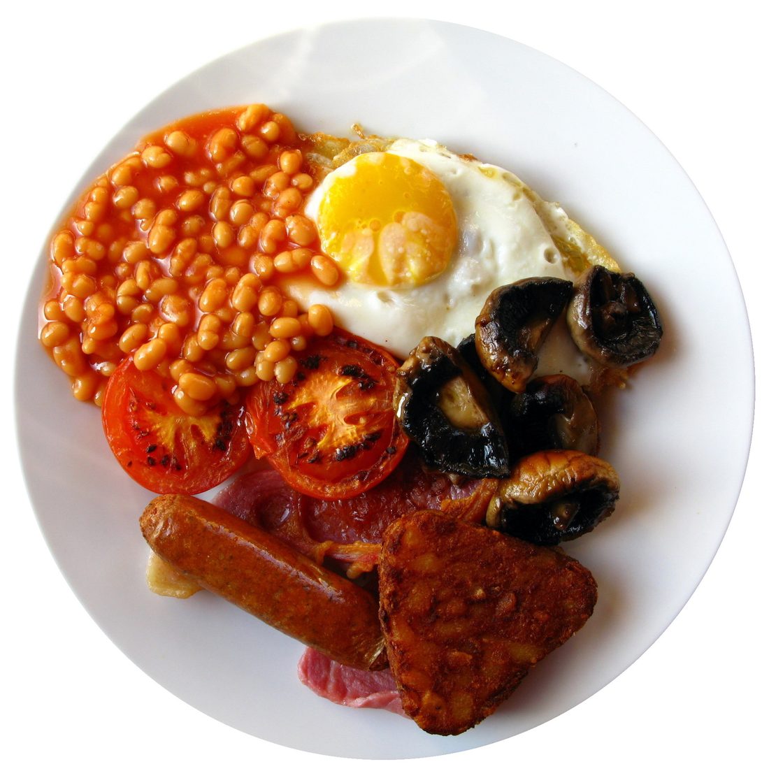 A cooked breakfast shot from directly overhead: beans, a fried egg, mushrooms, tomato, sausage and bacon on a white plate