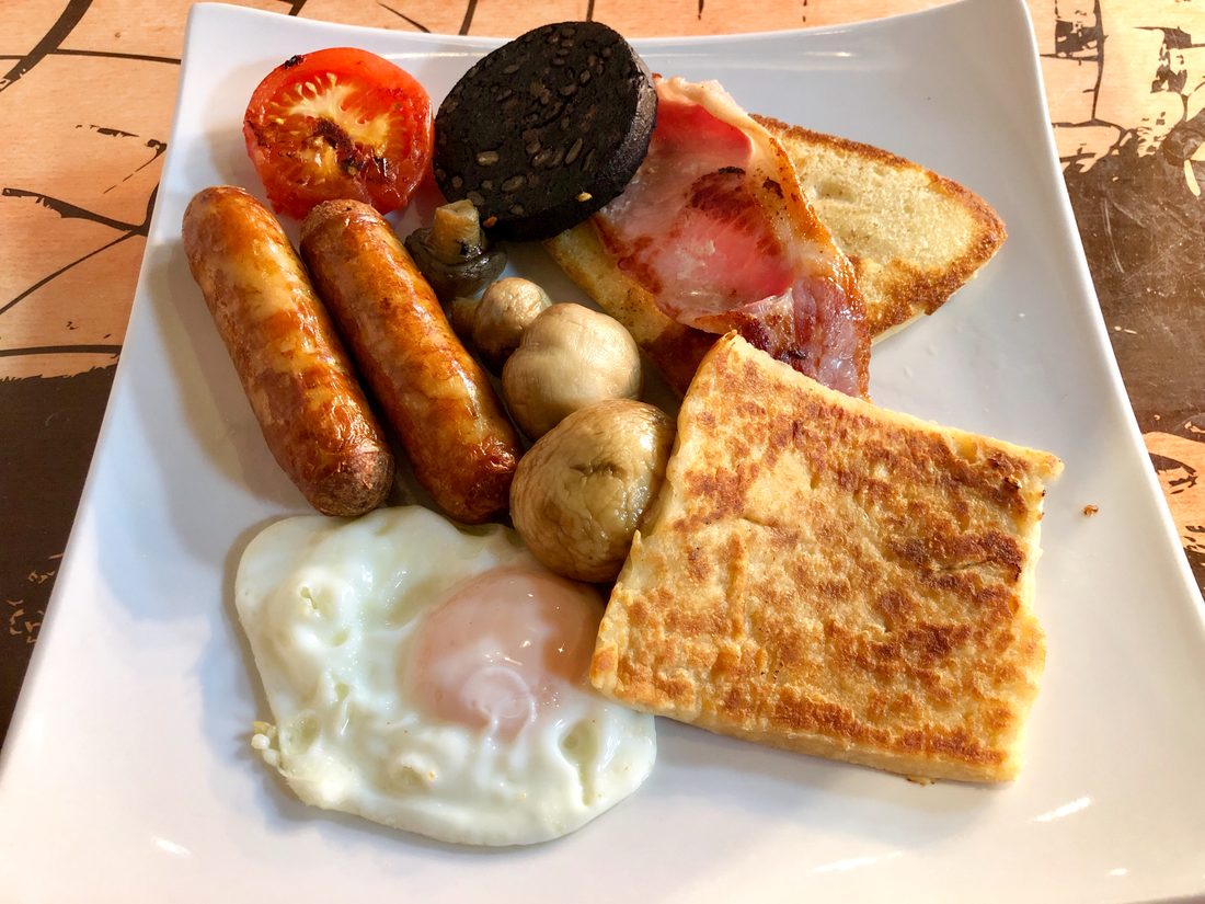 A fried breakfast plated with sausages, black pudding, bacon, egg and fried bread