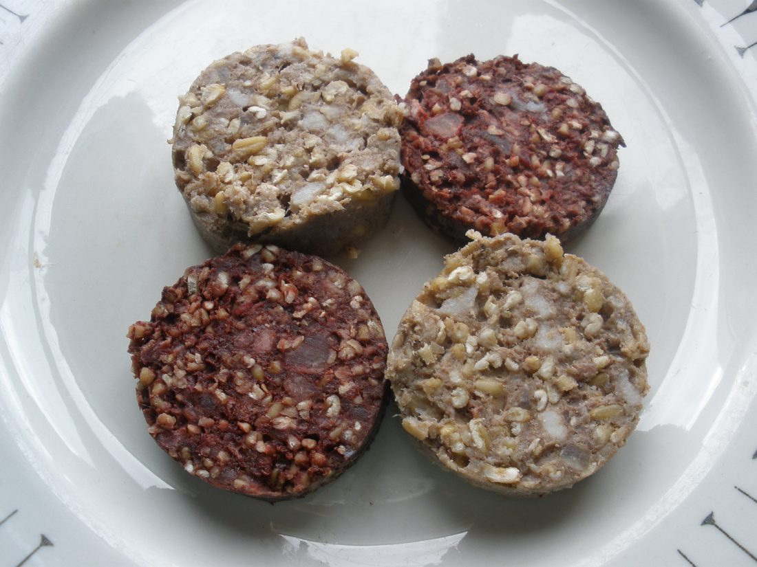 Rounds of white and black pudding on a plate, the white one pale and flecked with oatmeal