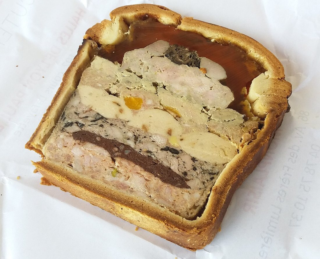 A slice of pâté en croûte from Lyon: golden crust, layers of pale forcemeat and inlaid meats, and a band of clear jelly under the lid