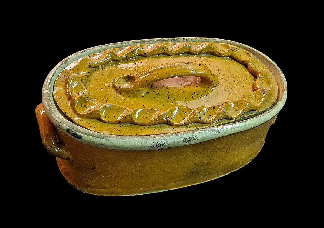 A lidded oval earthenware terrine glazed yellow and green, its lid molded with a twisted rim like a pastry crust, in the Musée alsacien, Strasbourg
