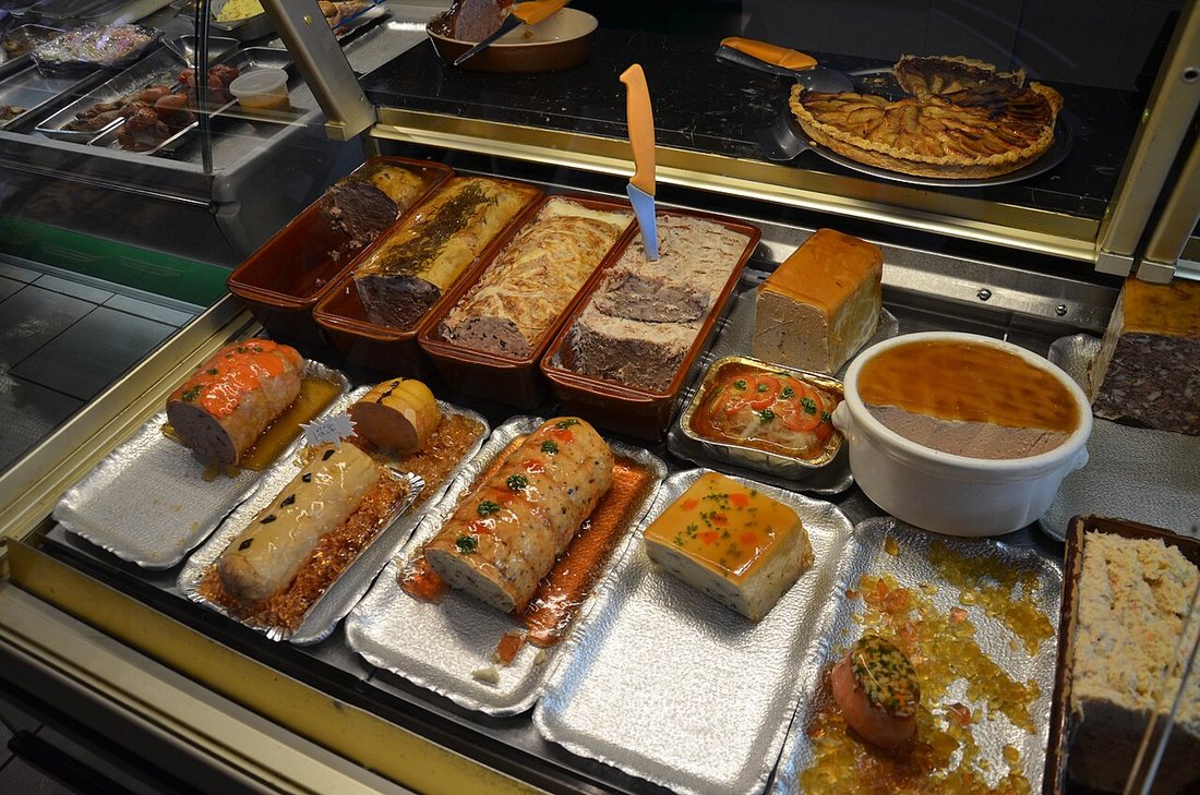 A French charcutier-traiteur's counter with rows of terrines, pâtés and a pâté en croûte in foil trays