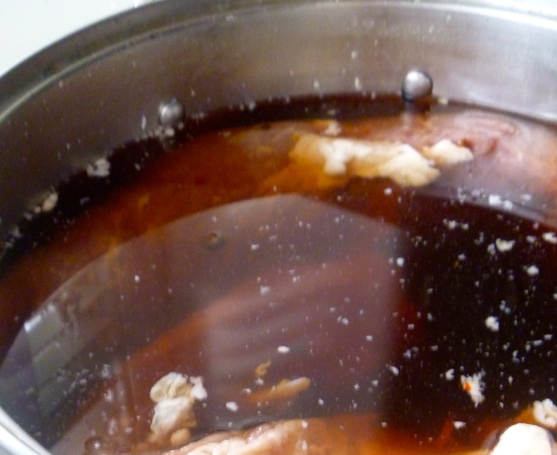 Beef submerged in dark curing brine in a stainless pot, fat and spice floating at the surface. This liquid is what a butcher calls the pickle, and there is no vinegar in it