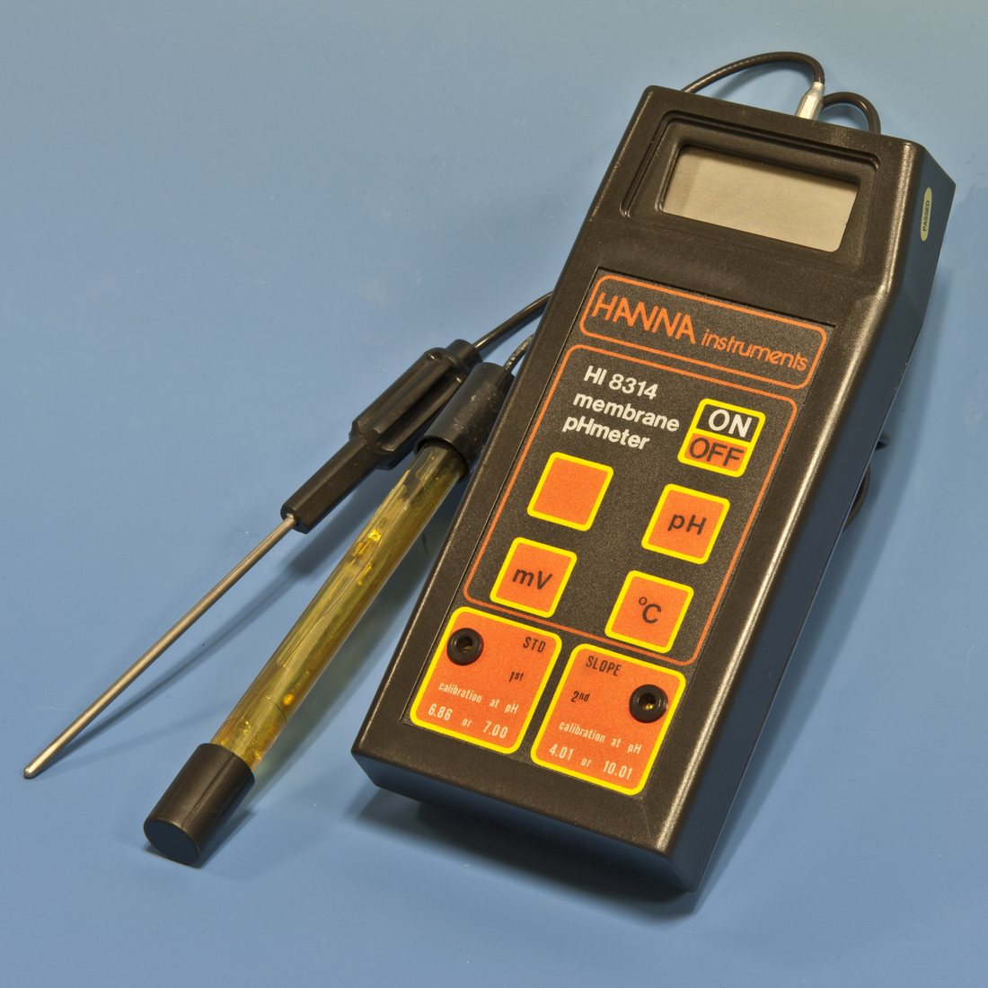 A handheld Hanna membrane pH meter with its glass electrode and temperature probe unplugged and laid beside it. This is the shape of the thing — a body, a replaceable probe on a lead, and two buttons you will actually use