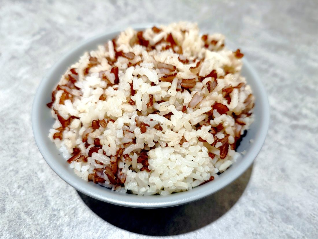 A side-by-side of brown rice and white rice in two bowls, the brown grains visibly tan and the white grains pale
