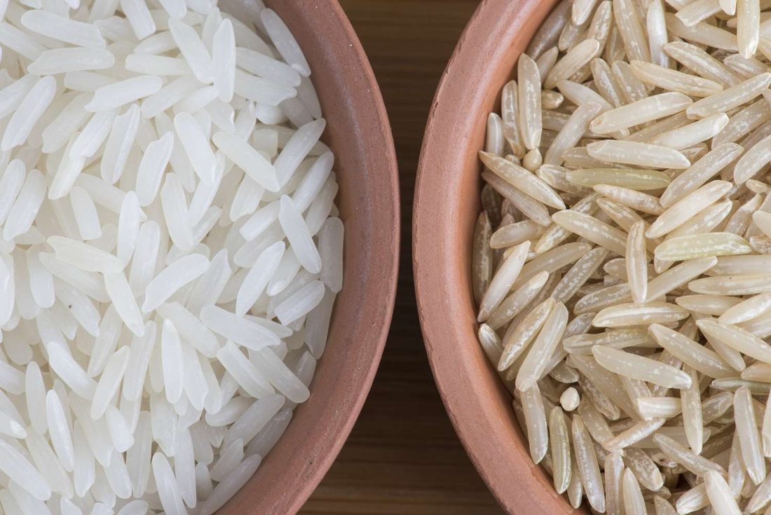 A bowl of cooked brown rice beside a bowl of white rice, the brown grains showing the intact tan bran layer