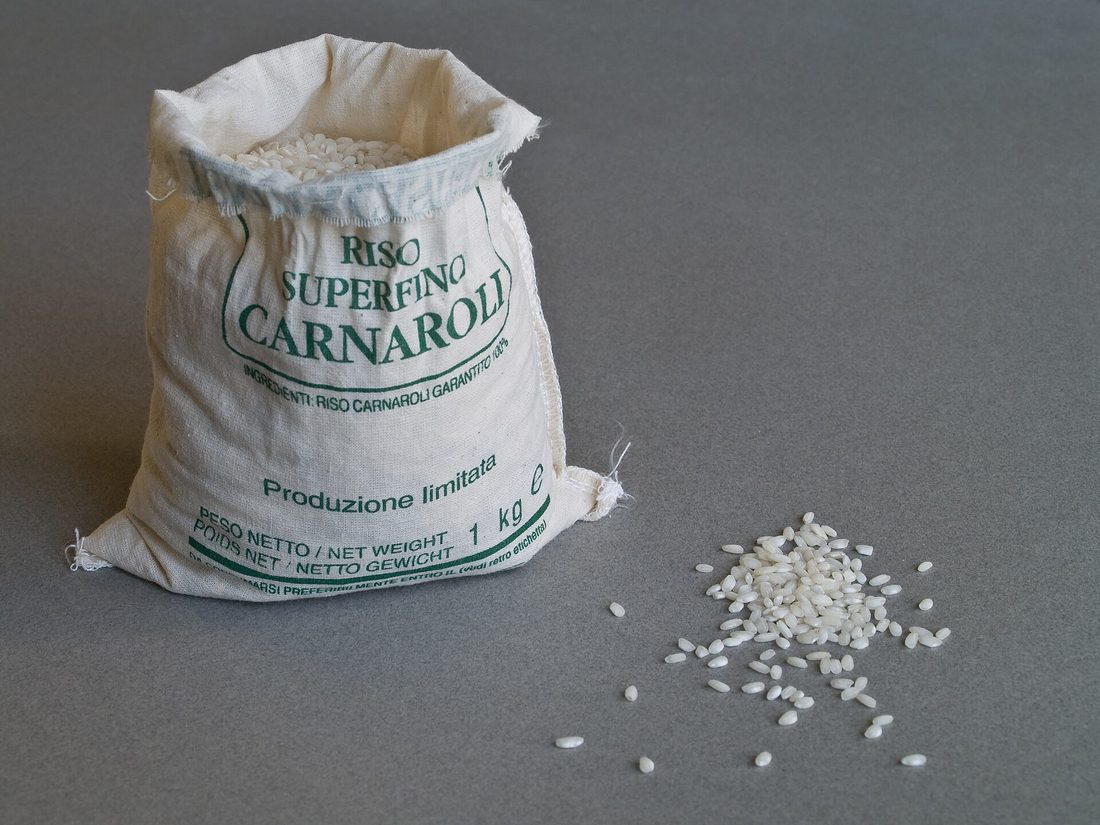 A hand holding plump pearly Arborio rice grains, showing the opaque white center of each short fat grain