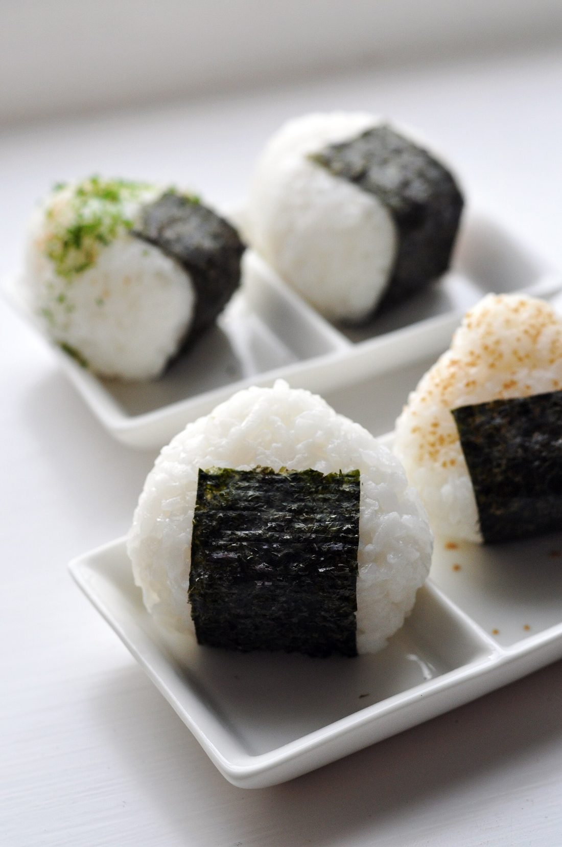 A neatly filled Japanese bento — a mound of white rice, a triangular nori-wrapped onigiri, and small savory sides in their compartments