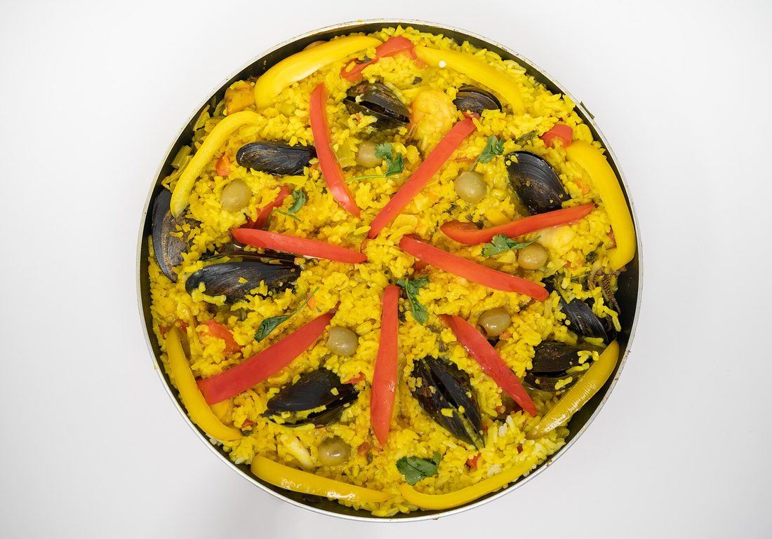 A wide Valencian paella pan straight off the fire — a thin even layer of saffron-gold rice, no stirring marks, being scraped to show the toasted socarrat crust stuck to the bottom