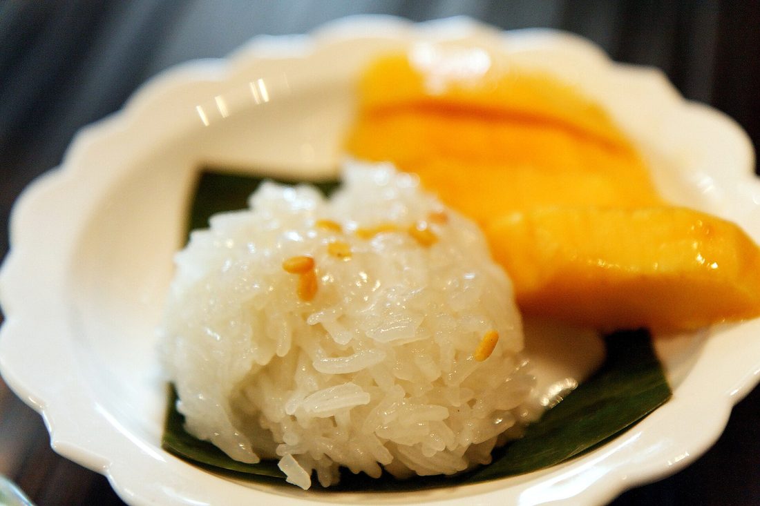 A woven bamboo basket of steamed Lao sticky rice, translucent and glossy, with a hand pinching off a ball of it