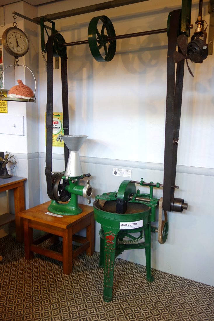 A surviving meat mincer made by the Enterprise Manufacturing Company of Philadelphia, alongside a green Buffalo chopper, in a museum of technology — Enterprise's tinned cast-iron choppers were the household name in American kitchens for generations.