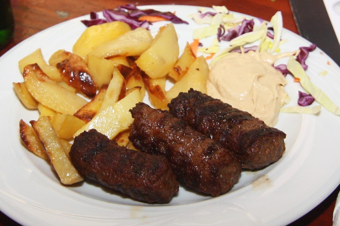 Mici (mititei) with mustard — Romania's caseless grilled rolls, a local crystallization of the same Ottoman grill tradition as ćevapi.