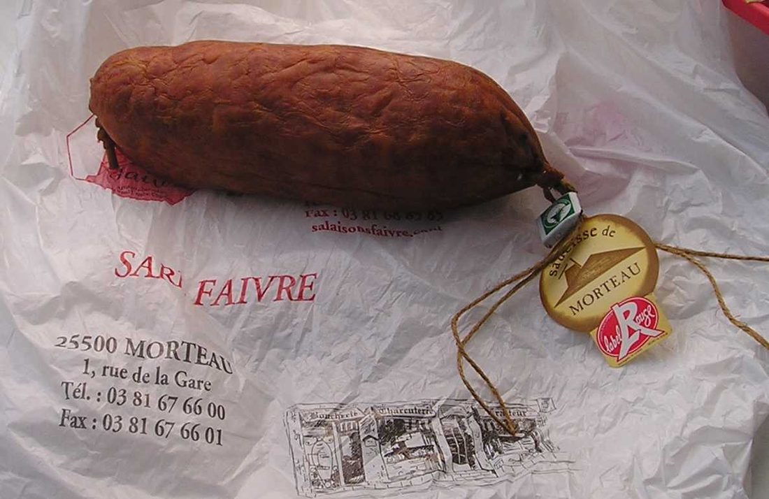 Saucisse de Morteau, sealed at one end with its wooden peg (cheville) — smoked in a Franche-Comté tuyé over conifer and juniper.