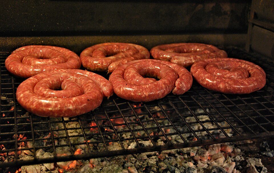 Boerewors in its unbroken spiral coil on the braai — the coriander-forward South African sausage, legally at least 90 percent meat.