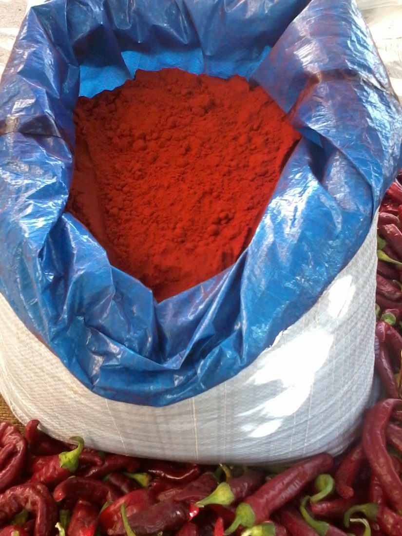 Spanish pimentón, milled from the smoked dried peppers heaped around it — not just color or heat but a functional antioxidant that slows the fat’s oxidation, and not interchangeable with Hungarian paprika.