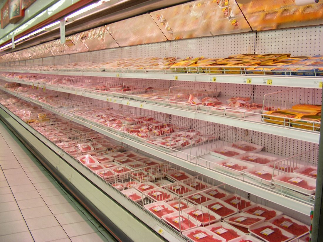 The commodity meat aisle that replaced the counter — case-ready, shrink-wrapped and consistent, cut and packed far away by a handful of companies.