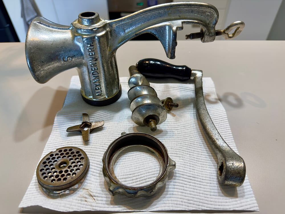 A grinder with its plate and four-wing knife laid out on the towel beside it — the tools a cold, coarse grind depends on