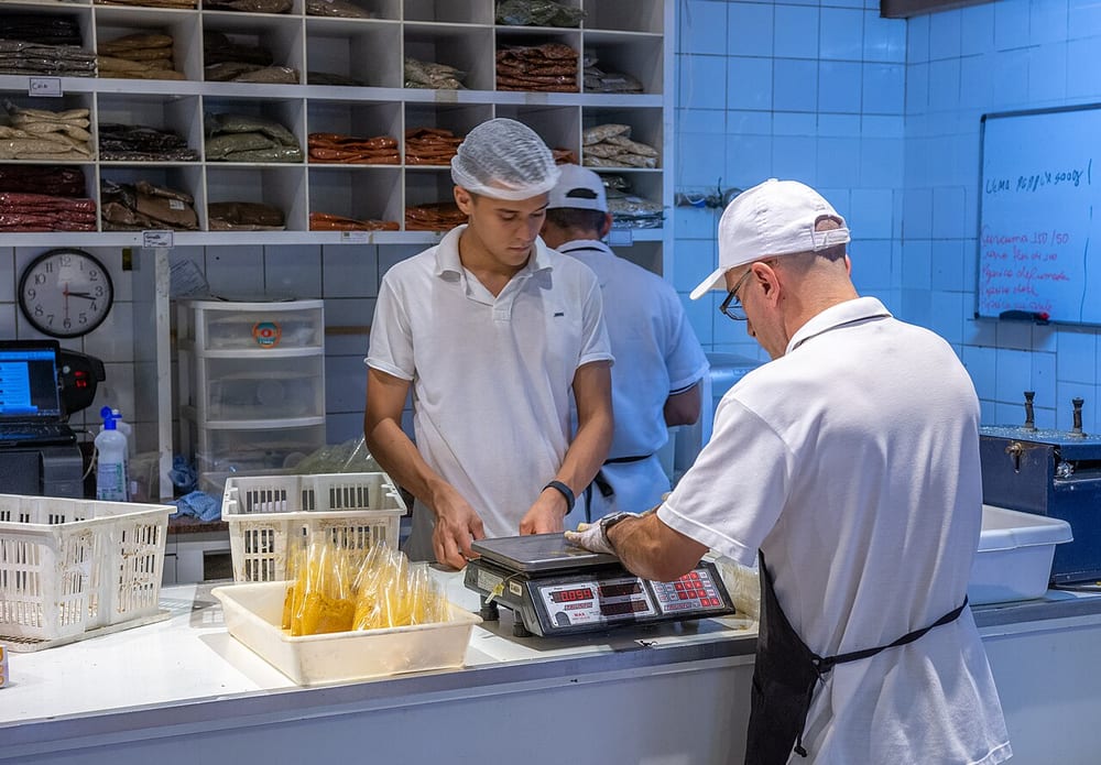 A butcher's case seen end-on: fresh coils, poached white sausages, a hanging rack of dried salami and a sliced blood pudding all within three feet of each other. Every class on this page is in this one photograph, and nothing about their appearance tells you which is which