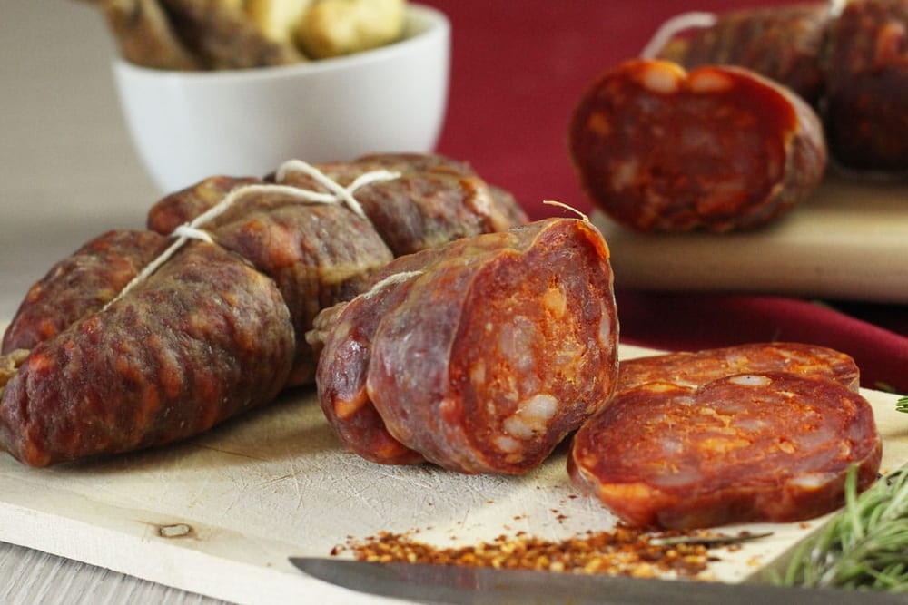 A cut face of coarse dry sausage showing distinct white cubes of back fat against dark red lean, the fat definition a recipe's grind and ratio are actually aiming at