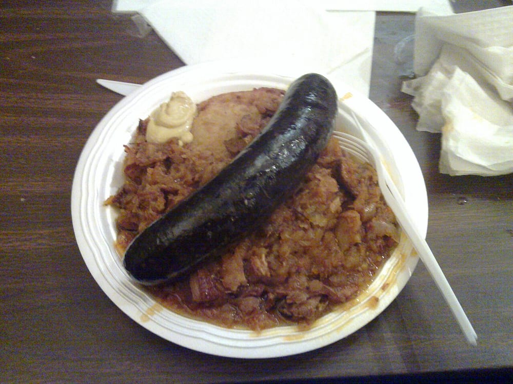 A length of boudin noir sliced open beside sautéed apple, the cut face dark and completely smooth with no visible grain at all