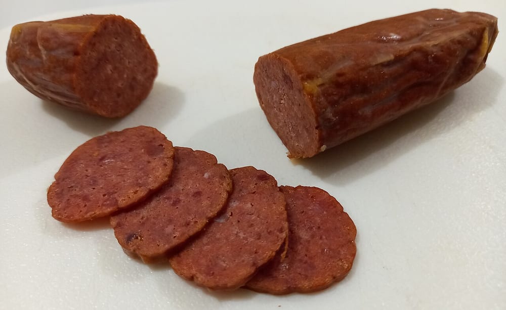 A dry-cured Spanish chorizo vela partly sliced, the coins deep brick red with clean white fat, laid out on a board with bread