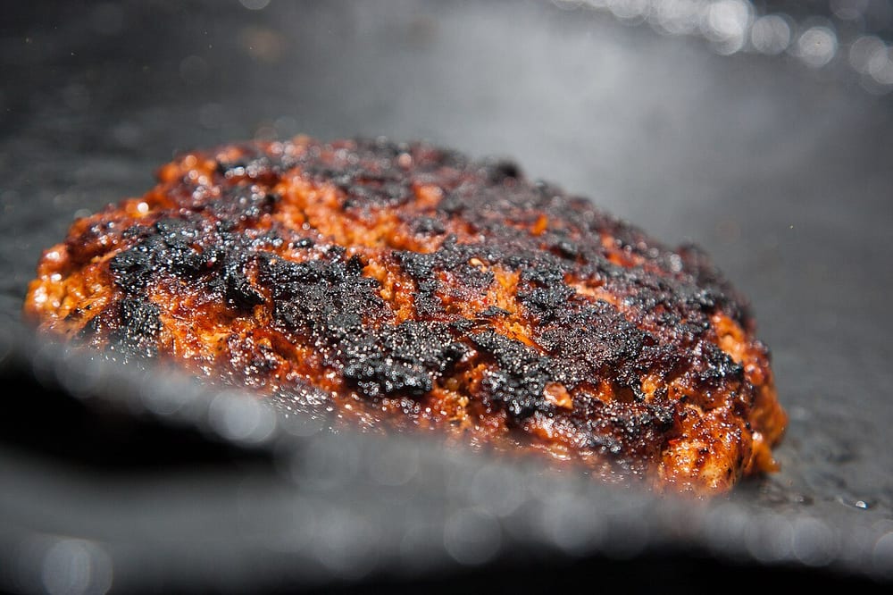 Fresh Mexican chorizo crumbling and browning on a griddle, loose and deep-red, no link structure left at all