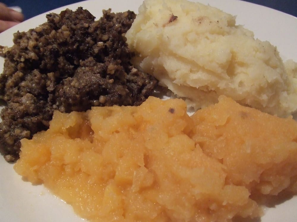 A haggis split open at the table, the steaming oat-and-offal filling spilling out of the natural casing beside neeps and tatties