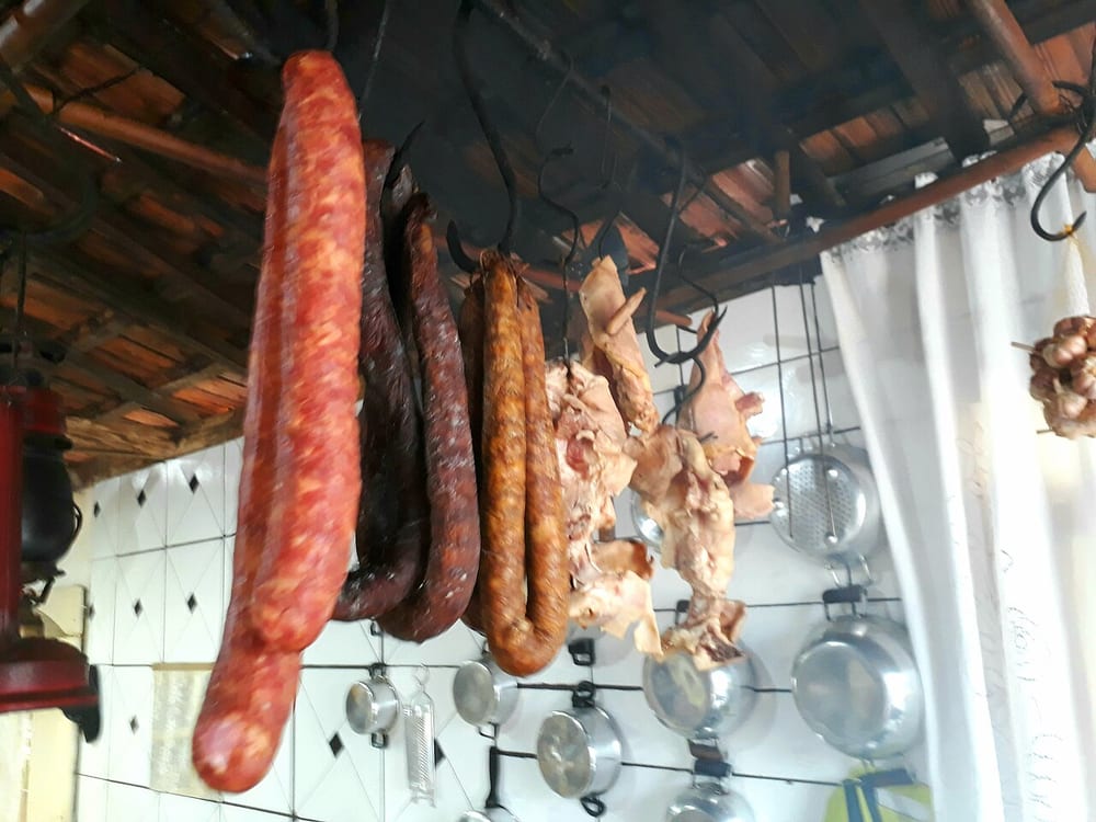 Coils of linguiça hanging in a smokehouse, the casings burnished orange-red from paprika and smoke