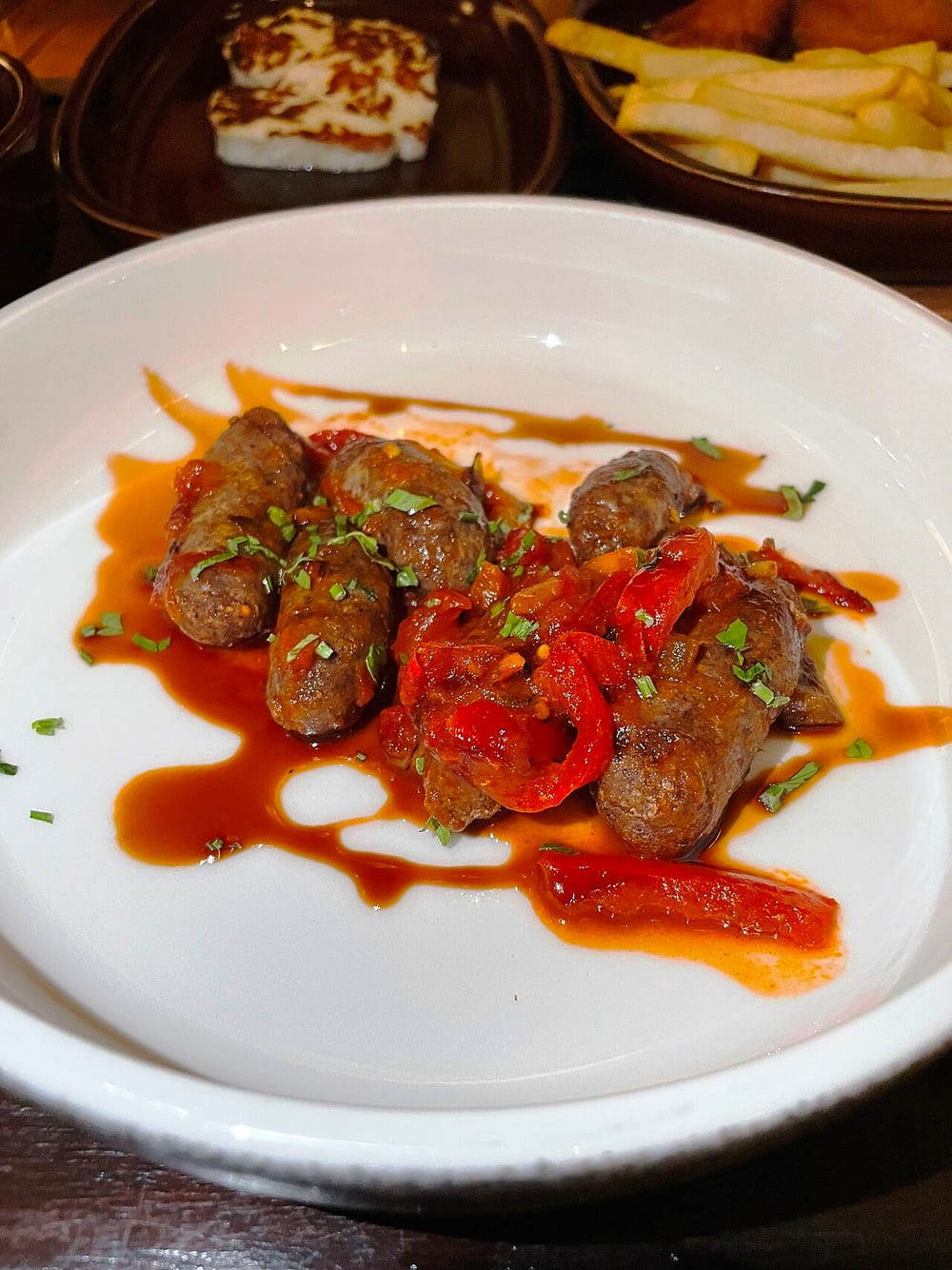 Small plump makanek plated glossy in their sauce, the Levantine breakfast sausage