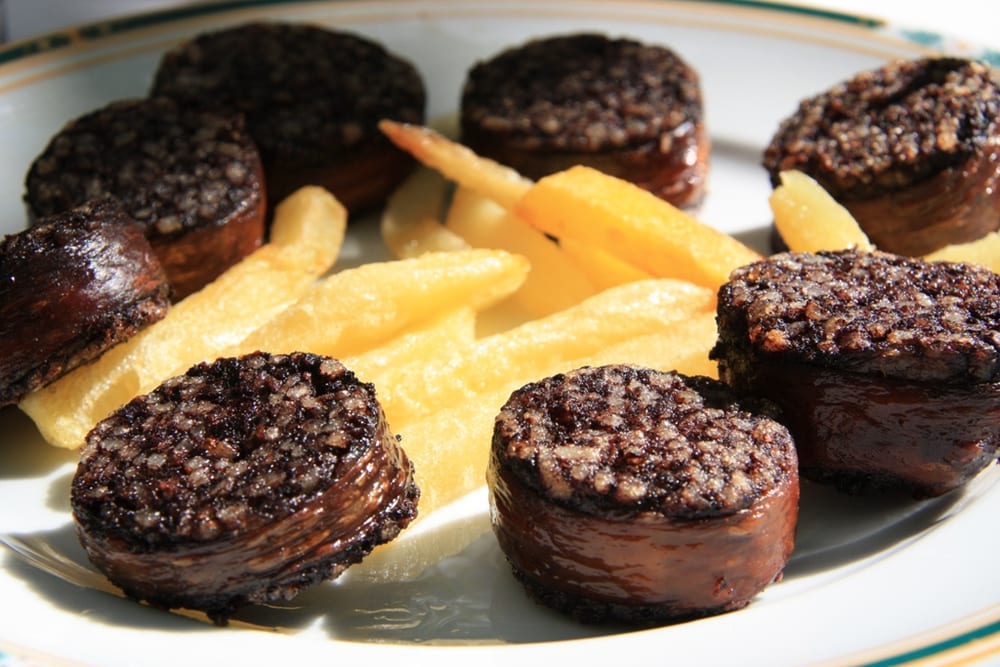 A round of morcilla de Burgos crumbling apart in a hot pan, individual grains of rice clearly visible in the dark crumb