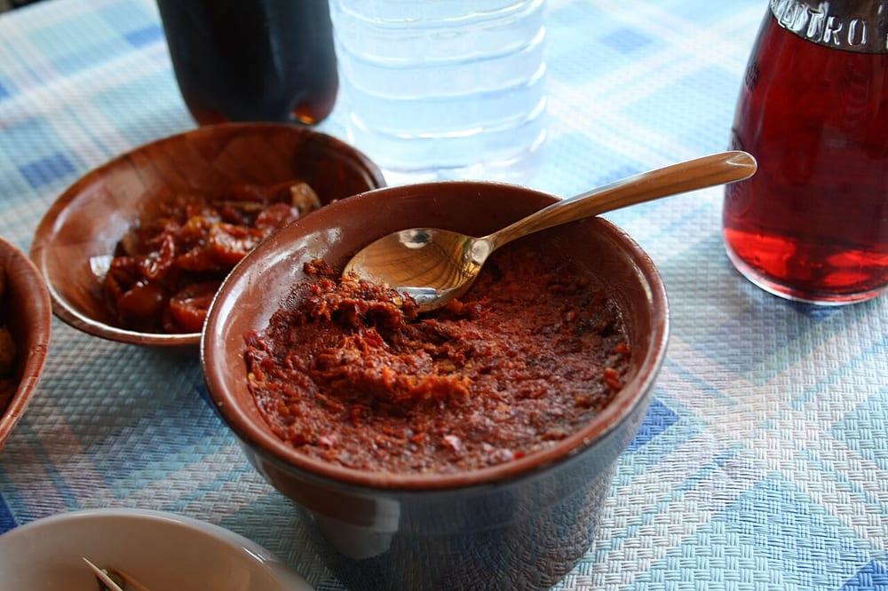 A jar of 'nduja with a spoon lifting a glossy scarlet spoonful, so soft it slumps back into itself