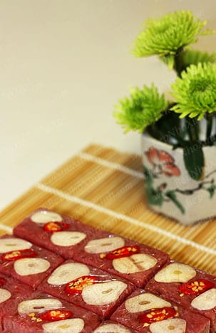 Small pink cubes of nem chua unwrapped from banana leaf, each topped with a slice of raw garlic and a sliver of red chili