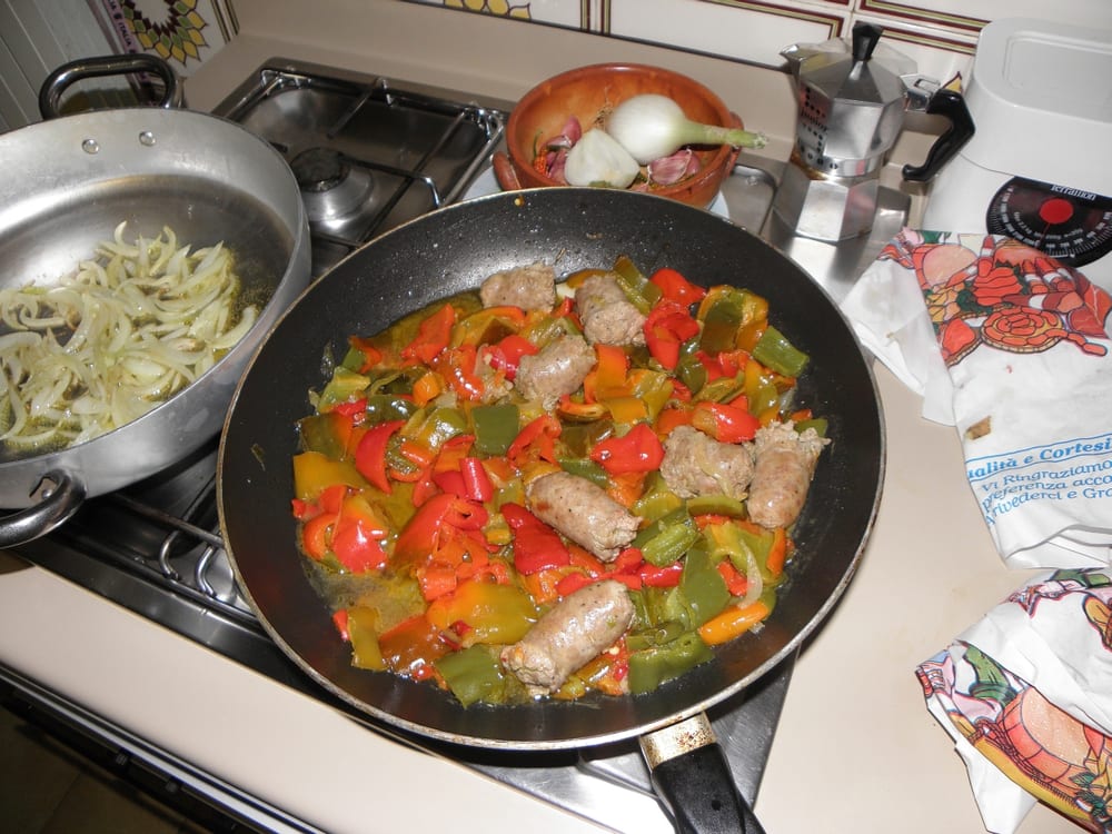 Fresh Italian salsiccia coiled in a pan with peppers, the coarse grind and whole fennel seed both visible through the casing