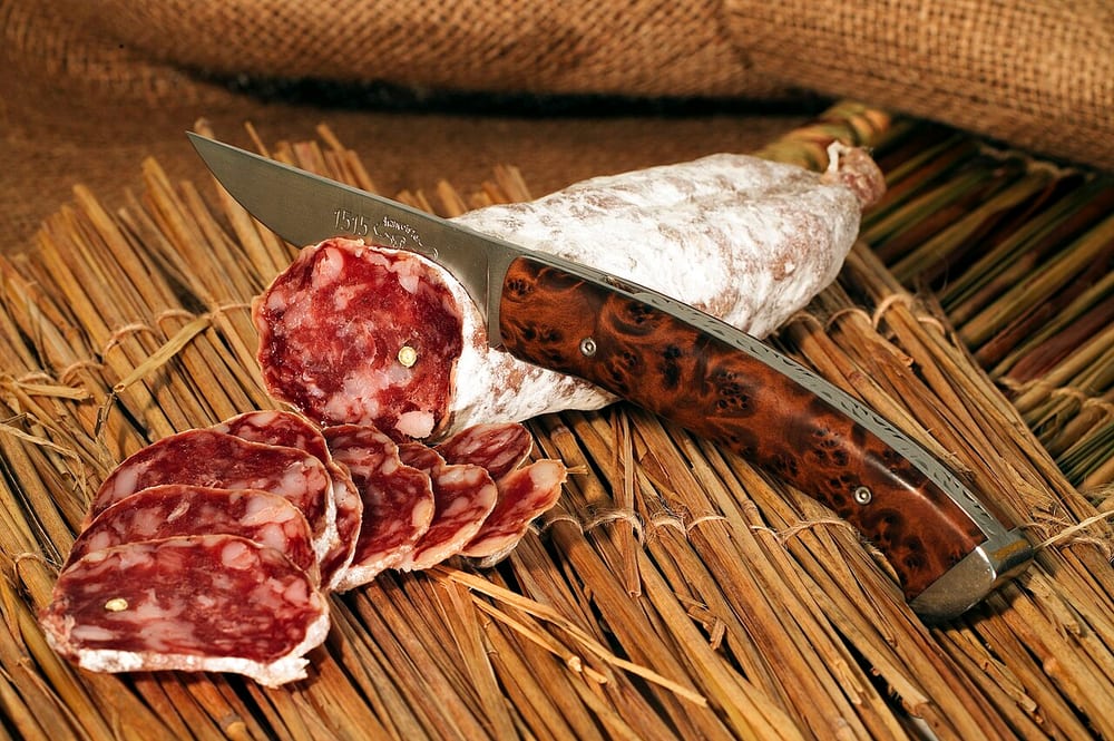 Saucisson sec hanging on strings in a cellar, chalk-white with mold bloom, one cut open to show coarse dark meat and clean white fat