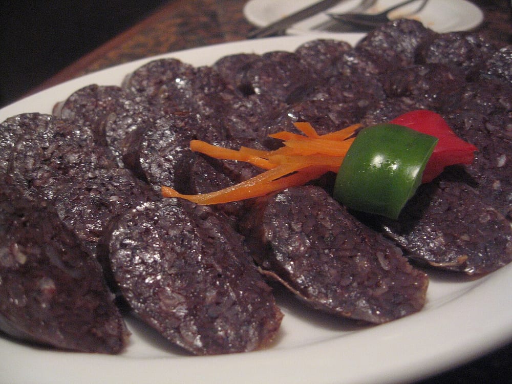 Steamed soondae sliced into coins on a paper-lined tray, the dark filling shot through with translucent glass noodles