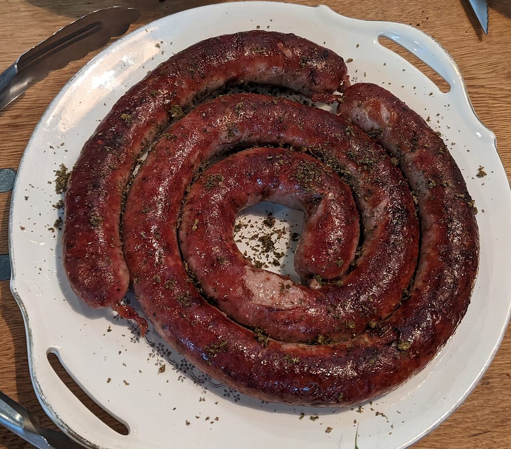 A wide coil of Saucisse de Toulouse in a serving dish, the coarse-ground spiral browned and held in shape
