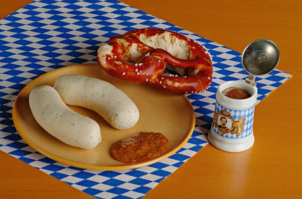 Two pale Weisswurst on a Bavarian plate with a soft pretzel and sweet mustard