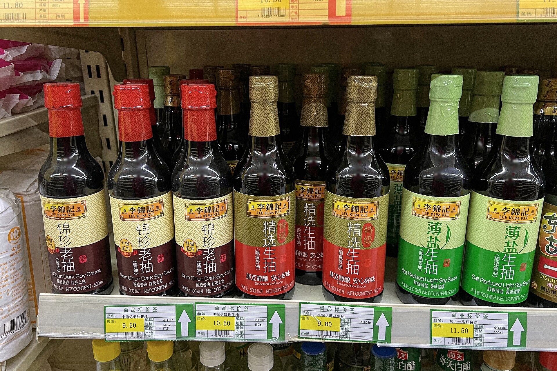 A supermarket shelf of Chinese soy sauces — a dozen labels in red, gold and green, light and dark side by side