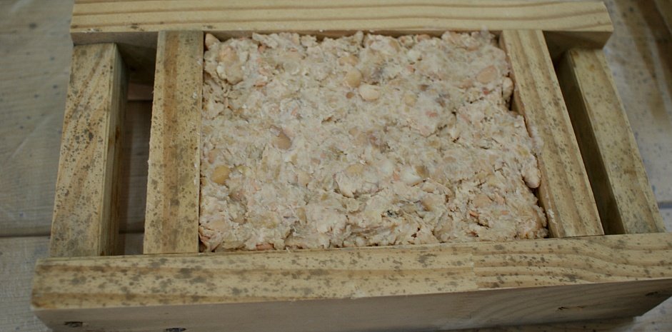 Pale mashed soybeans being pressed into a rectangular wooden mould to form a meju block